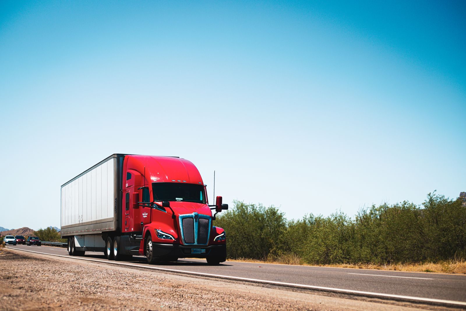 Red Kenworth semi hauling a dry van trailer down an open American highway